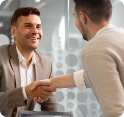 Homem de terno sorrindo enquanto aperta a mão de um cliente, ilustrando a fidelização e o encantamento no atendimento.